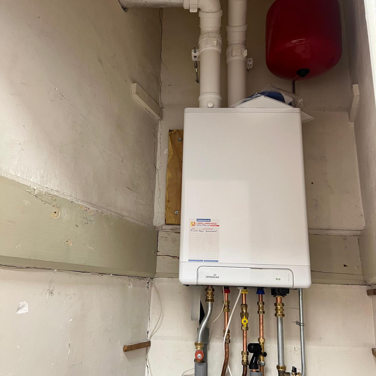 Onderhoudskaart met handgeschreven data, geplakt op een Intergas cv-ketel in een meterkast